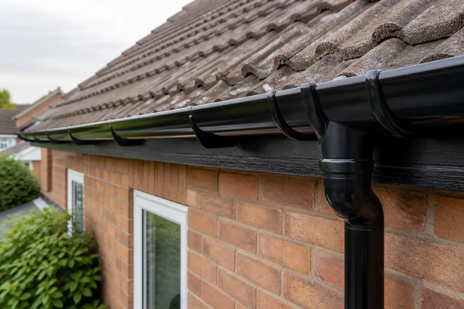 New black uPVC gutter, fascia and downpipe installed along the eaves of a tiled roof